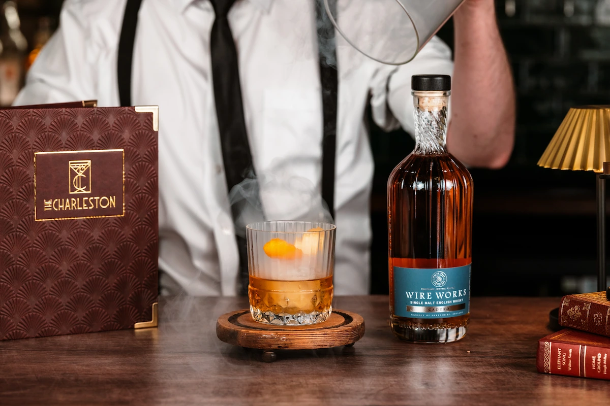 A bartender pulling the lid off the smoky old fashioned cocktail